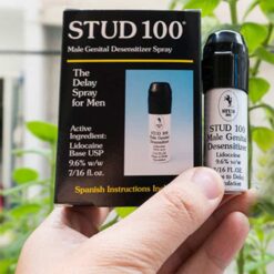 Tay cầm hộp và chai xịt Stud 100 chính hãng Anh Quốc giữa nền cây xanh - Nhà thuốc Trung Thắng